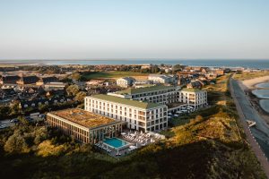 Luftaufnahme vom Arosa Sylt Hotel am Strand, im Hintergrund sind andere Häuser und das Meer zu sehen