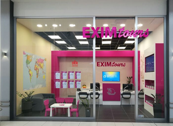 Blick in ein Reisebüro von EXIM Tours mit pinken und grauen Möbeln, eine Weltkarte an der Wand und zwei Arbeitsplätzen