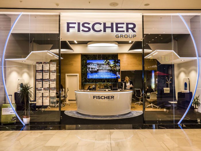 Blick von außen in eine Filiale eines Fischer-Reisen- Reisebüros in Tschechien. in der Mitte ein großer Counter mit Fischer Reisen Logo, an den Schaufenstern hängen Angebotszettel