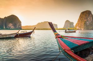 bunte Longtailboote in Thailand, im Hintergrund sind Kalkfelsen zu sehen