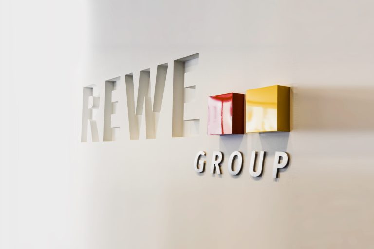 Rewe group Logo an einer weißen Wand