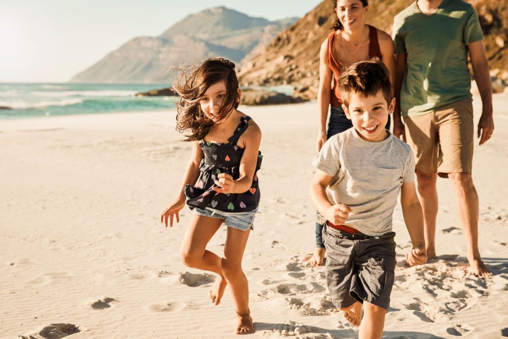 Familie mit einem Mädchen und einem Jungen am Strand, die Kinder laufen lachend vor den Eltern weg