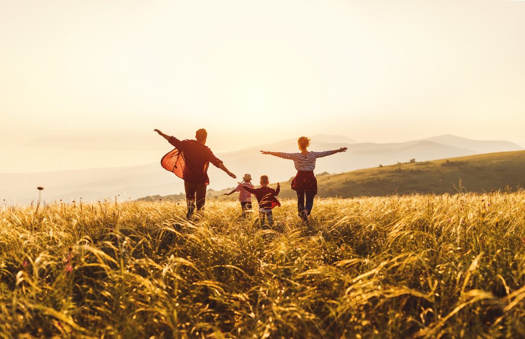 Glückliche Familie: Mutter, Vater, Kinder Sohn und Tochter laufen und springen in der Natur bei Sonnenuntergang