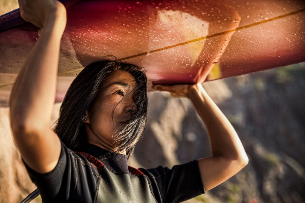 Asiatische Frau mit einem Surfbrett schaut in die Ferne