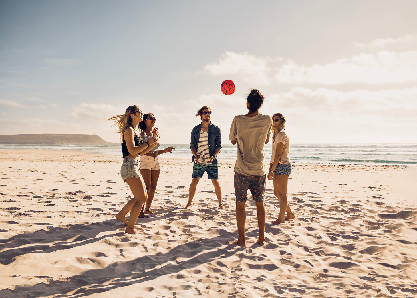 fünf junge Menschen spielen Beachvolleyball an einem Strand