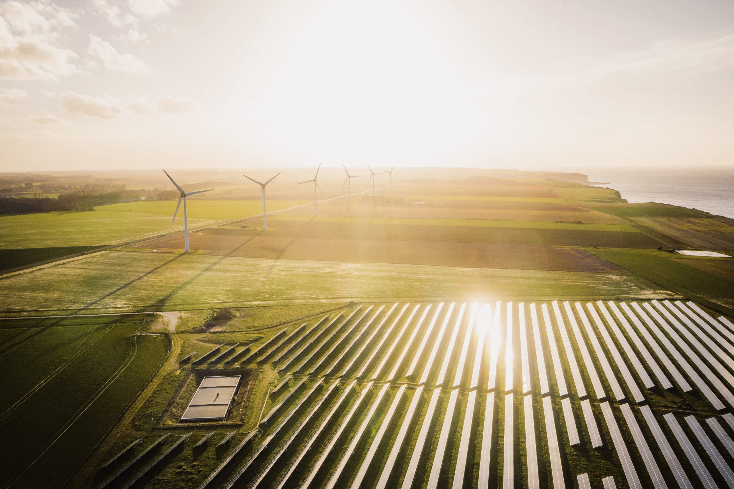 Windmühlen und Sonnenkollektoren auf einer grünen Wiese in der Nähe des Meeres. Konzept für erneuerbare Energien. Grüne Energie zur Reduzierung der Kohlendioxidemissionen.